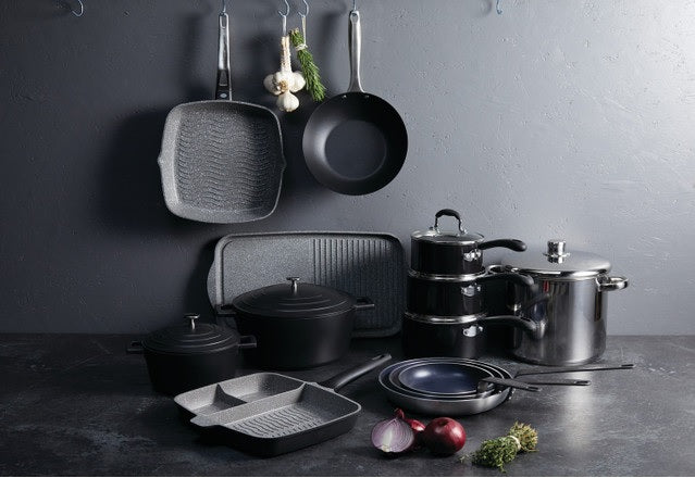 Melns katls ar vāku no lietā alumīnija kopā ar pannām un virtuves traukiem, piemērots gatavošanai uz plīts